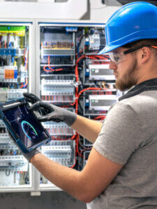 Electrician with tablet. Working at switchboard. Digital tools in use.